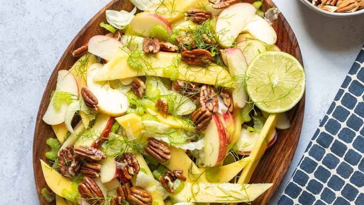 Colorful mango and pecan salad on a wooden plate.