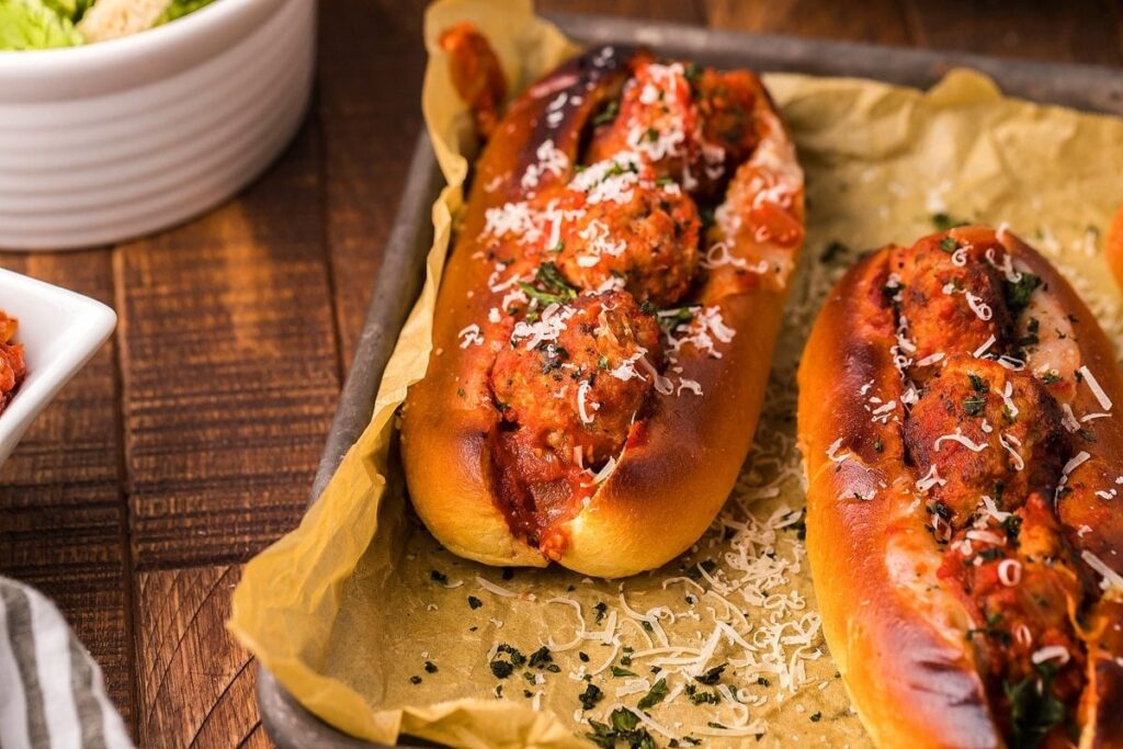 Two hot dogs with sauce and salad on a baking sheet.