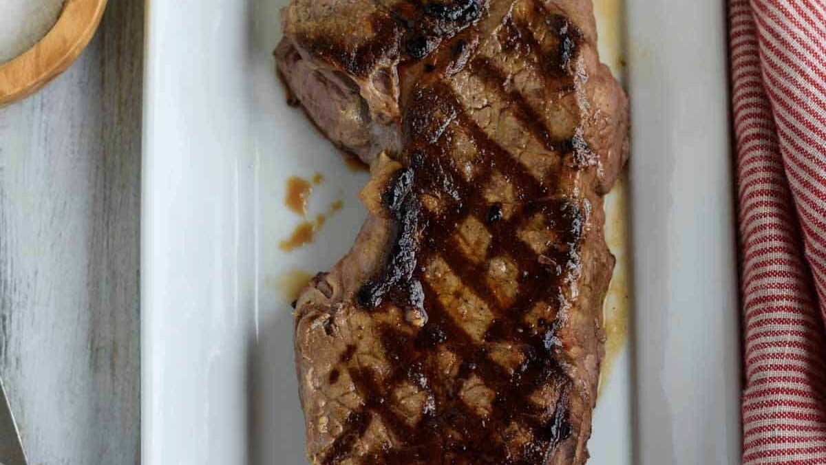 A dinner party main featuring a steak on a white plate, perfectly seasoned with salt and pepper.