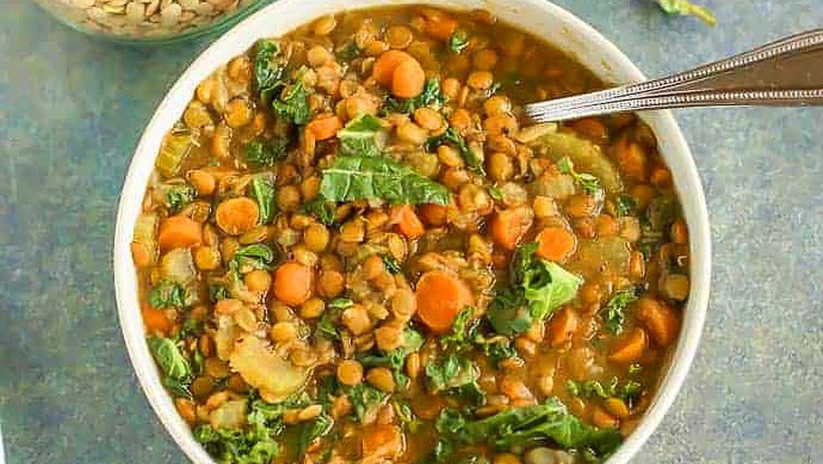 A bowl of lentil and kale soup with a spoon.