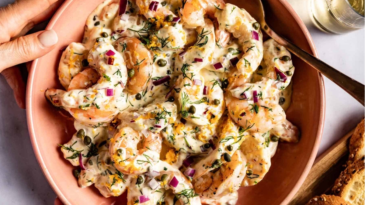A hand holding a fork indulges in a bowl of shrimp salad for dinner.