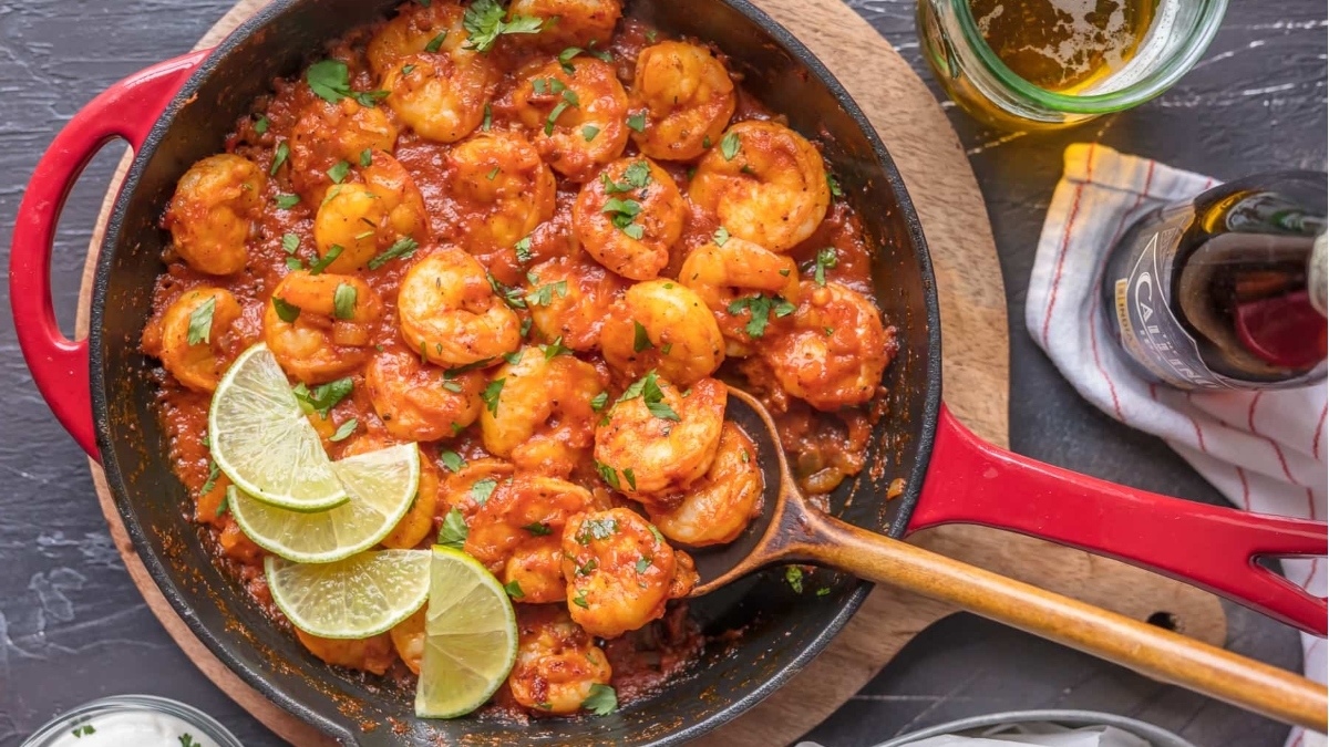 A delectable shrimp dinner, cooked to perfection in a skillet with a flavorful sauce and accompanied by zesty lime wedges.