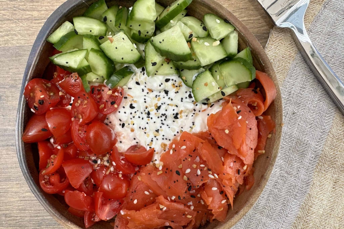 A healthy bowl with salmon, tomatoes, cucumbers and a fork.