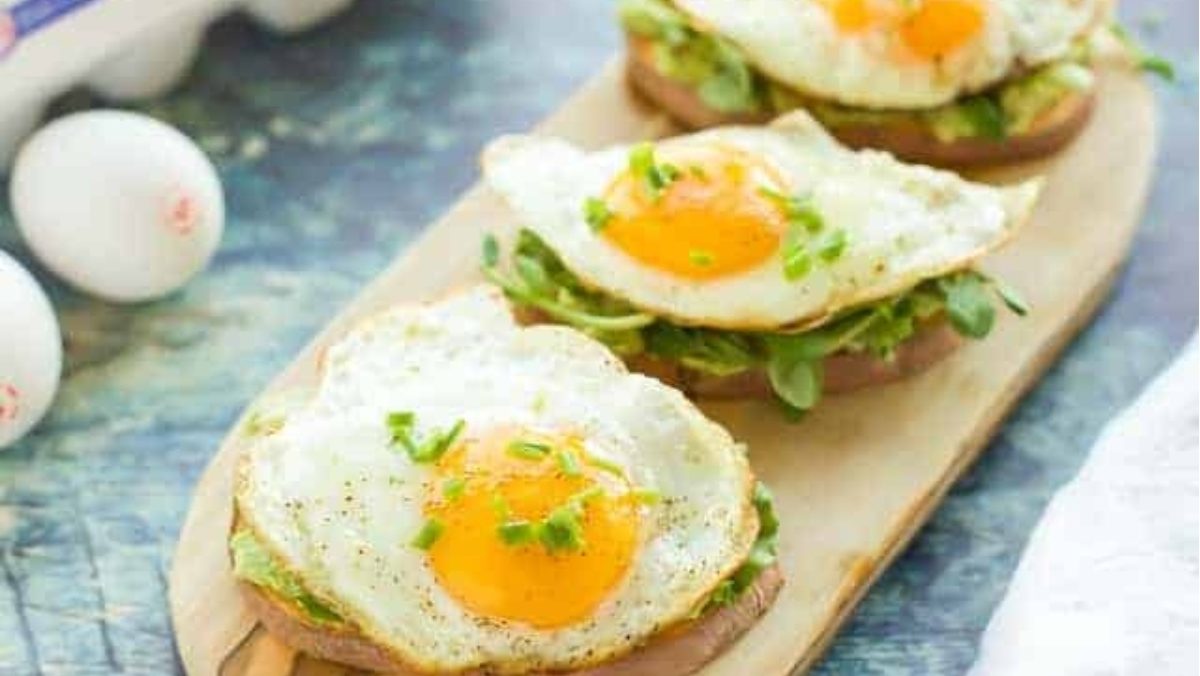 vocado toast with eggs on a wooden cutting board.